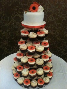 A tower of cupcakes with alternate orange gerberas and white roses with a top cutting tier with a posy of orange gerberas and roses