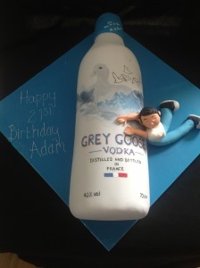 a Grey Goose vodka bottle on blue iced board and man draped over side of bottle