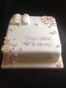 a square white cake with scattered pink, yellow and lilac flowers and butterflies with a bible in the top left corner
